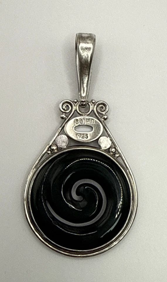 SAJEN BLACK NIGHT SWIRL PENDENT: SAJEN BLACK NIGHT SWIRL PENDENT The Sajen Black Night Swirl Pendant is a stunning piece of fine jewelry crafted from 925 sterling silver. It features a unique swirl design that adds a touch of eleganc