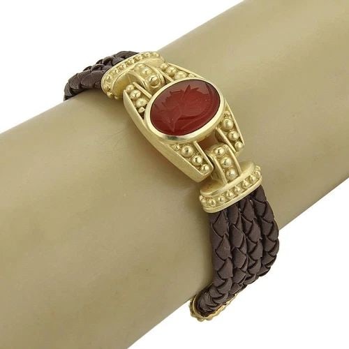 JUDITH RIPKA CARNELIAN GOLD BRACELET INTAGLIA 18K YELLOW BRAIDED MULTI-CORD BAND: JUDITH RIPKA CARNELIAN GOLD BRACELET INTAGLIA 18K YELLOW BRAIDED MULTI-CORD BAND The Judith Ripka Carnelian gold bracelet features a unique intaglio design with 3 strand braided brown leather braided 