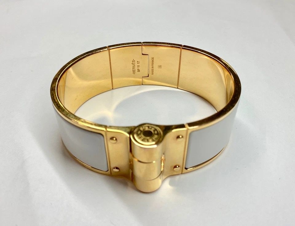 HERMES GOLD PLATED HINGED BRACELET WITH WHITE ENAMEL SP1117 (7 INCH) 78.8 GRAMS: HERMES Gold Plated Hinged Bracelet with White Enamel SP1117 You are bidding on a pre-owned HERMES Gold Plated Hinged Bracelet with White Enamel. The bracelet has scuffs and scratches from normal wear 