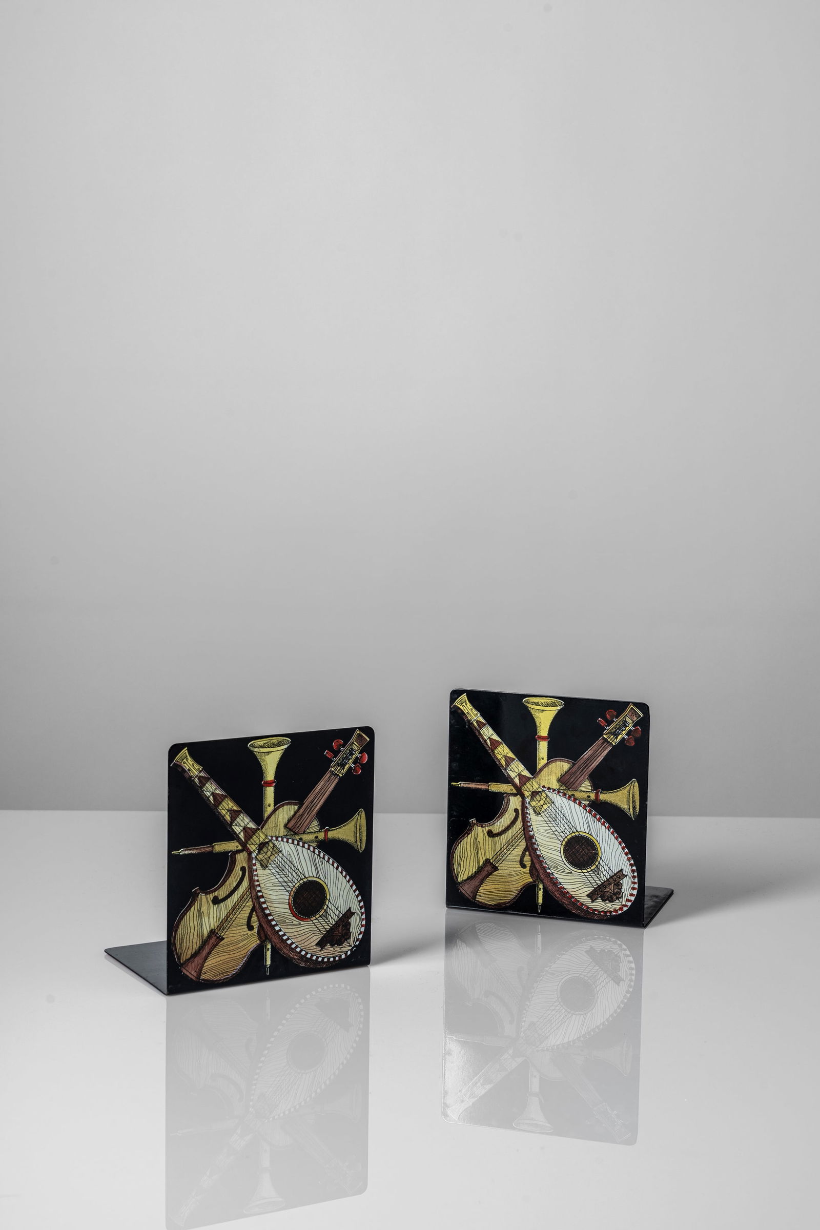 Piero Fornasetti (Milano 10/11/1913 - Milano 09/10/1988) - Pair of bookends 'strumenti musicali',: 15 x 10 x 13,5 cm Pair of bookends with silk-screen 'strumenti musicali' printed decorationdeisgned in 1960 circametal screen printed and clothoriginal logo FORNASETTI - MILANO, MADE IN ITALY on the u