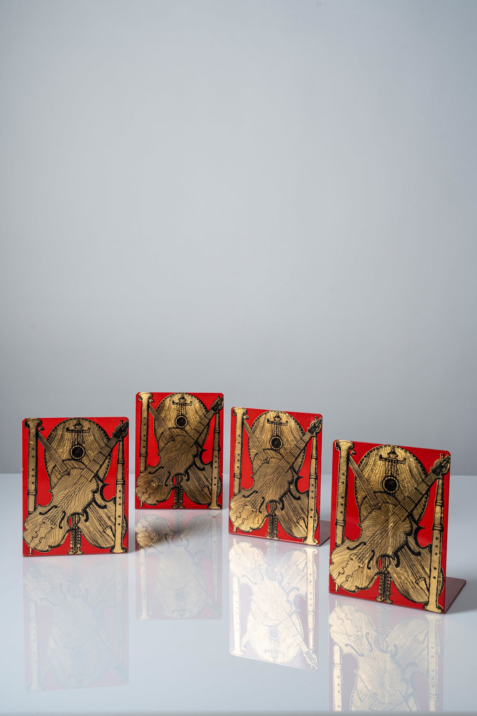 Piero Fornasetti (Milano 10/11/1913 - Milano 09/10/1988) - Set of four bookends, 'musical: 20,4 x 15 x 13 cm Set of four bookends with silk-screen 'musical instruments' gold leaf printed decorationdeisgned in 1960 circametal screen printed, clothoriginal logo FORNASETTI - MILANO, MADE IN IT