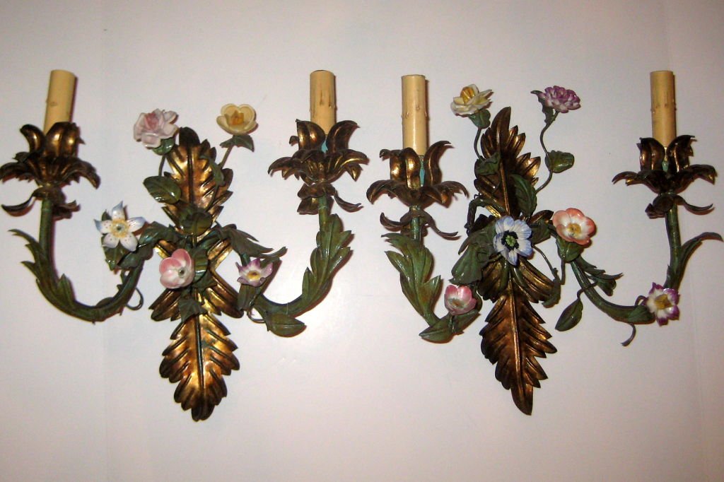 PAINTED TOLE SCONCES WITH PORCELAIN FLOWERS: A pair of turn of the Century Italian metal sconces with porcelain flowers. Rewired. Measurements Height: 11 in. Depth: 8 in. Width/Length: 13 in. This item ships from New York, NY