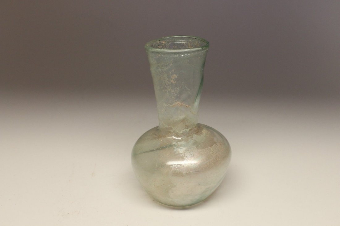 ROMAN GLASS BOTTLE - Middle East ca. 2nd - 3rd Century: A pale green tapered bulbous bodied bottle with a long tapered neck and a flared mouth. Raised scrolling pattern on surface of neck. Silvery iridescence surface patina on interior. Dimensions: 4" (10 