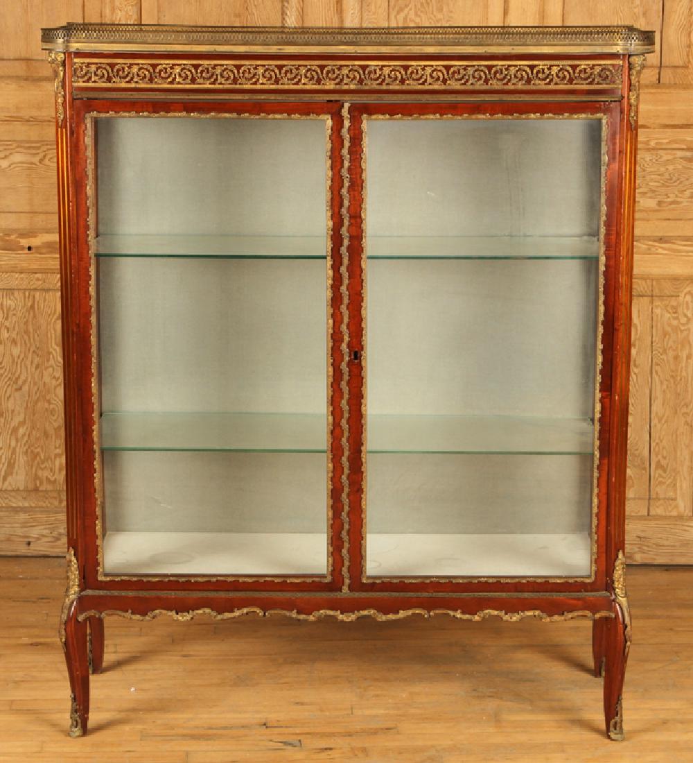 MAHOGANY BRONZE MOUNTED MARBLE TOP VITRINE 1940: A mahogany bronze mounted marble top two door vitrine having glass shelves with a fabric covered back and illuminated interior circa 1940. Ht: 54" Wd: 43.5" Dpth: 16.5"