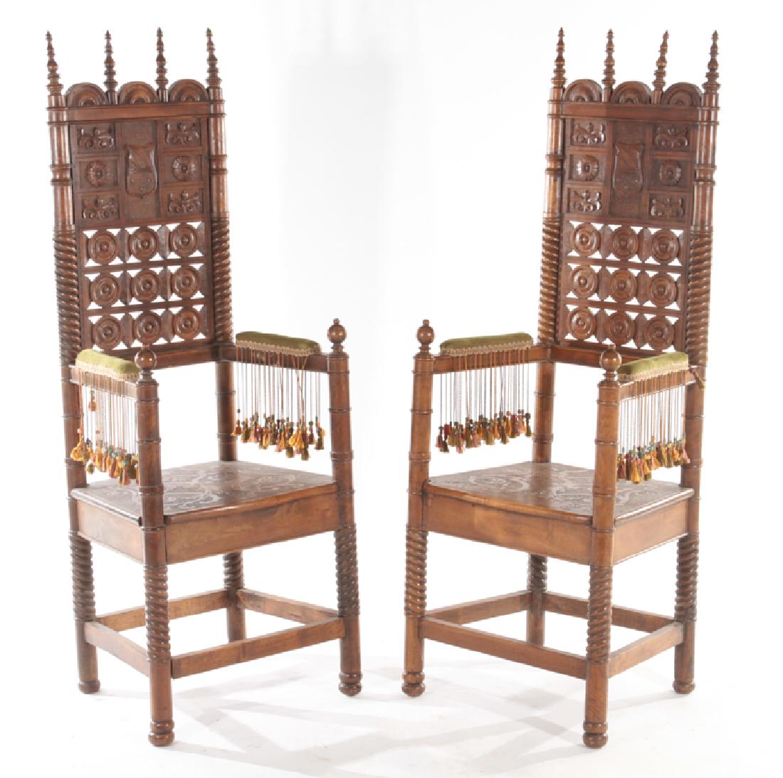 PAIR CARVED WALNUT MOORISH STYLE OPEN ARM CHAIRS: A pair of tall back carved walnut Moorish style open arm chairs circa 1900. Having heraldic carvings on back rest, twisted and turn supports and tassel decorated upholstered arm rests. Ht: 58.5" Wd: 2