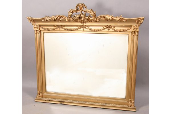 ANTIQUE GILT BEVELED FIREPLACE MANTLE MIRROR: Antique carved gilt mantle mirror with shaped cornice and scrollwork over a garland decorated frame circa 1920. Glass is beveled. Ht: 47" Width: 51" Depth: 3" ***PLEASE NOTE: All property shall be pai