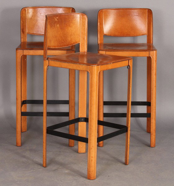 SET OF 3 MID CENT MODERN BRIDLE LEATHER BAR STOOL: Set of three mid century modern stitched bridle leather bar stools circa 1970. Each having simple back and seat supported on tall legs with metal box stretcher. Ht: 36" Width: 15.5" Depth: 15"