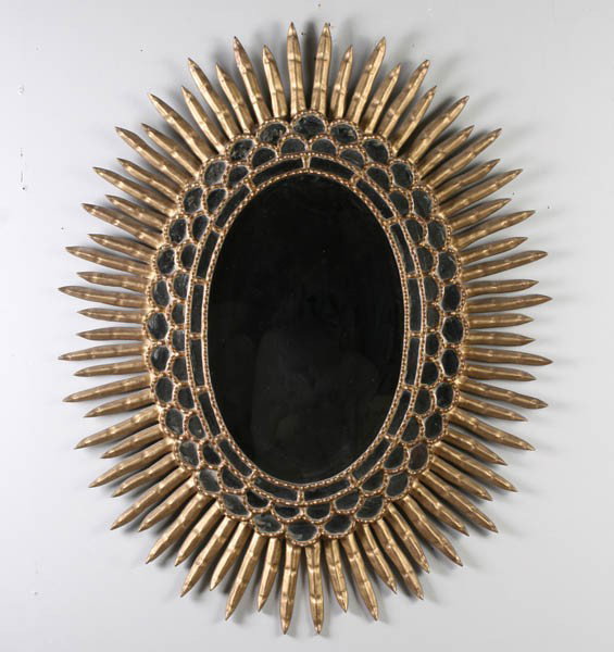 SUNBURST STYLE PAINTED WOOD AND GESSO MIRROR: A large sunburst style gold painted wood and gesso oval mirror having stylized 'rays' and stepped frame. Ht: 40" Width: 32"