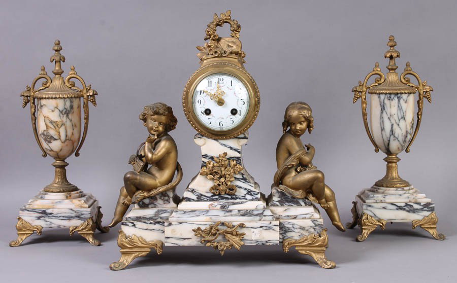 ANTIQUE FRENCH GARNITURE CLOCK SET MARBLE METAL: Antique French garniture clock set having male and female putti flanking marble and metal clock circa 1910. With two classically inspired urns with grape clusters. Ht: 14" Width: 14" Depth: 6"