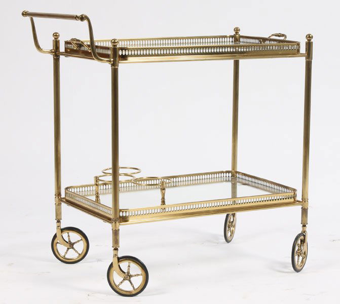 BRASS GLASS DRINKS SERVING CART C.1970: A brass drinks cart having galleried glass tray top over a lower shelf with bottle supports all raised on casters circa 1970. Ht: 28" Width: 26" Depth: 15"