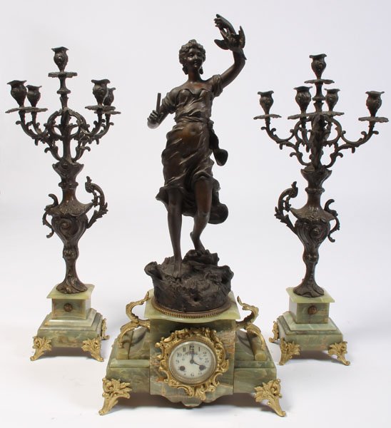 3-PC WHITE METAL ONYX GARNITURE CLOCK SET: A three-piece bronze, white metal and onyx garniture clock set having a standing woman holding fowl and a porcelain clock face. Pair garnitures: 29.25" x 10" x 10". Ht: 30.25" Width: 15" Depth: 7.5"