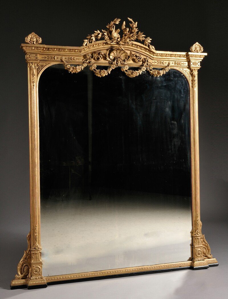 ANTIQUE VICTORIAN GILTWOOD FRAMED MANTLE MIRROR: An American Victorian giltwood framed mantle mirror having a central crest above an egg and dart molded frame. With pendant floral garlands extending over the mirror from a central shell-form crest. D