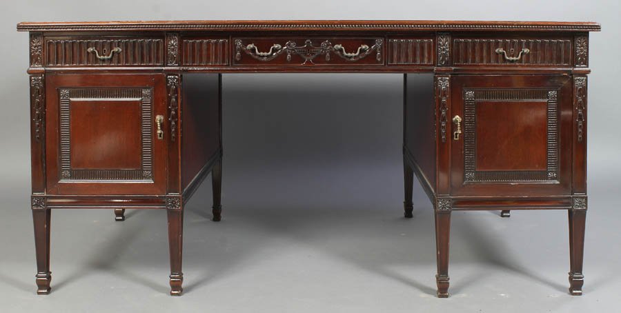 3 PART HEPPLEWHITE STYLE ANTIQUE ENGLISH DESK: Three-part Hepplewhite style English mahogany flat top desk circa 1910. The top case having three drawers, the center drawer with urn and swag carving. The two pedestals each having a single door, ope