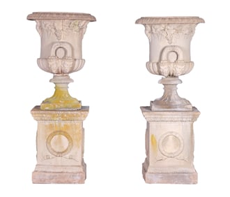 67" PAIR OF CAST STONE GARDEN URNS WITH FIGURAL HANDLES AND GRAPE LEAF DECORATION. THE BASES