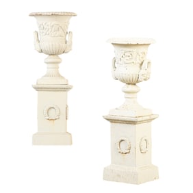 PAIR PAINTED CAST IRON GARDEN URNS HAVING FIGURAL HANDLES RESTING ON SEPARATE WREATH DECORATED BASE.