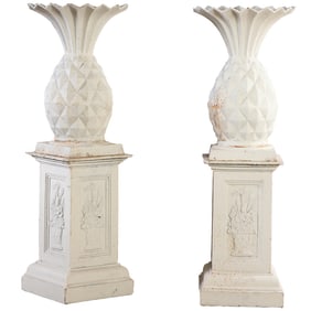 PAIR OF PAINTED CAST IRON PINEAPPLES SITTING ATOP A DECORATED CAST IRON BASE.