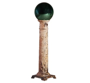 A CAST IRON PEDESTAL HOLDING A GLASS GAZING BALL.