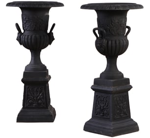 A DECORATED PAIR OF CAST IRON GARDEN URNS WITH HANDLES RESTING ON DECORATED BASES.
