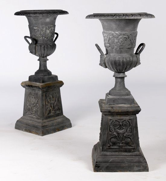 PR. CAST IRON GARDEN URNS LION FORM HANDLES: A pair of cast iron garden urns with egg and dart rims and lion form handles raised on decorated plinth base. Ht: 42" Dia: 19"