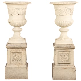 A PAIR OF CAPONIFORM PAINTED CAST IRON GARDEN URNS RESTING ON SEPARATE DECORATED PLINTHS.