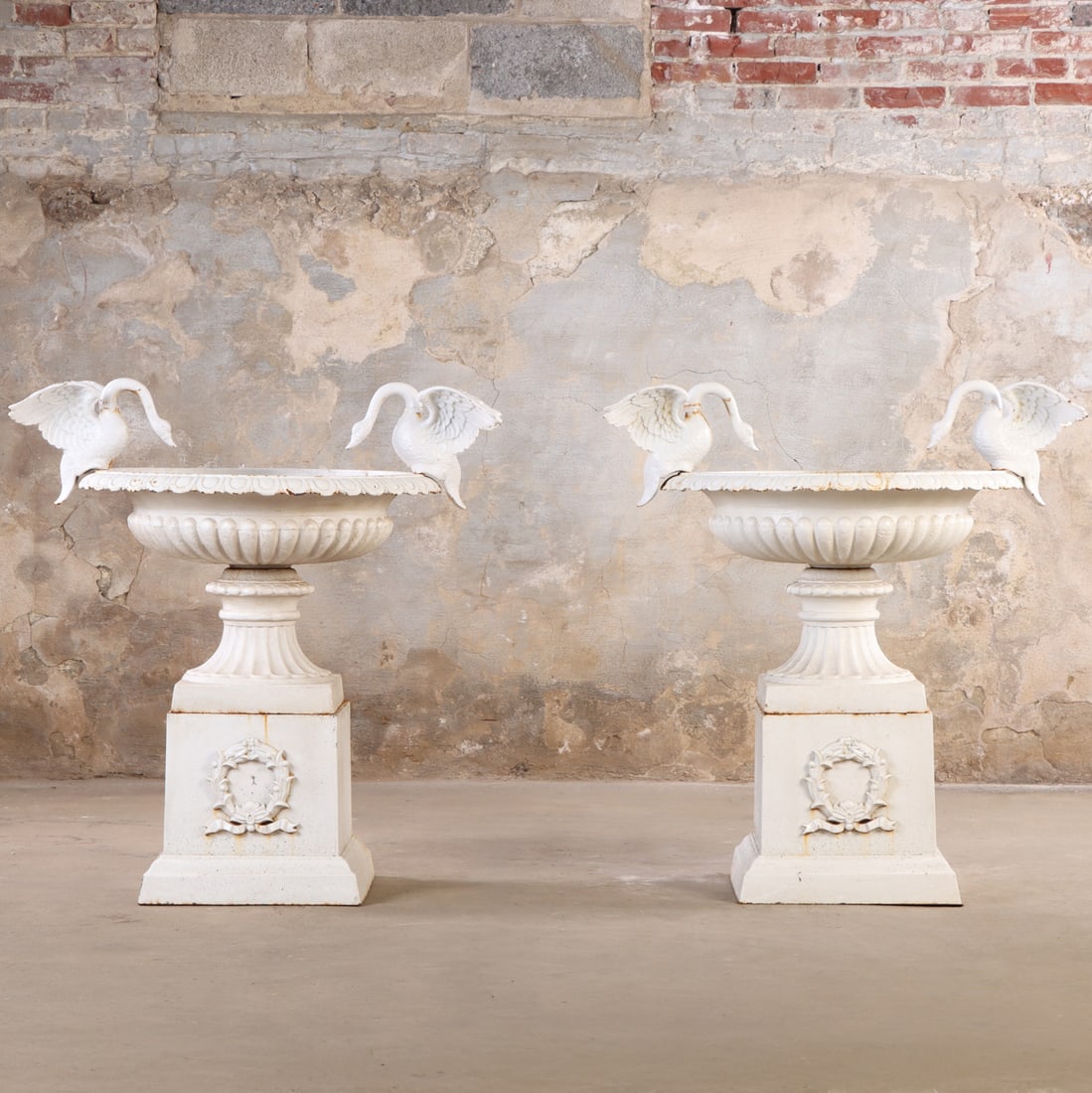 A PLEASING PAIR OF PAINTED CAST IRON GARDEN URNS HAVING FULL FIGURED SWANS AND RESTING ON A: A pleasing pair of painted cast iron garden urns having full figured swans and resting on a separate iron plinth with wreath decoration. Ht: 44" Wd: 39" Dpth: 31"