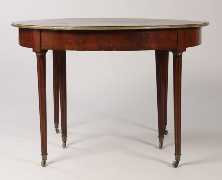 FRENCH LOUIS XVI STYLE BRASS TRIMMED DINING TABLE: A French Louis XVI style brass trimmed dining table supported on turned and fluted legs with bronze sabots and casters circa 1890. No leaves. Ht: 29" Dia: 44"