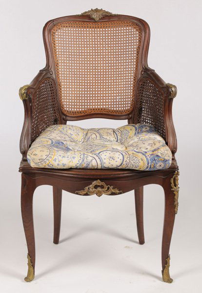 FRENCH L. XV LINKE MAHOGANY BRONZE ARM CHAIR: A French Louis XV Francois Linke carved mahogany and bronze mounted arm chair having caned back and continuous caned arms circa 1900. The arms with bronze decoration over shaped seat, supported on cab