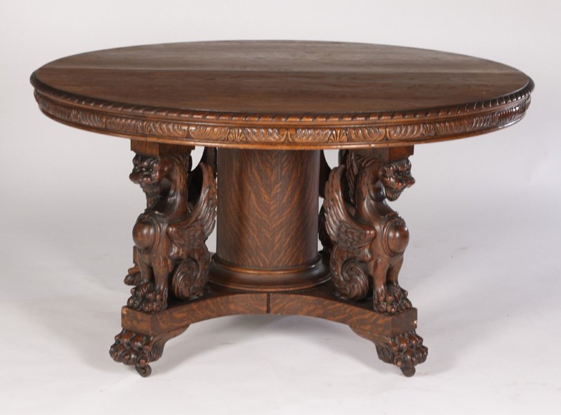 54" AMER. VICT GRIFFIN CARVED OAK DINING TABLE HASTINGS: A labeled Hastings 54" American Victorian griffin carved round oak dining table with seven original leaves circa 1890. The quatersawn top having a carved edge and skirt resting on a winged griffin spl