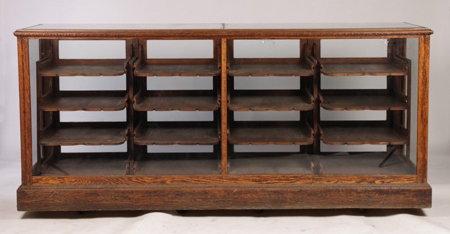 VICTORIAN ERA OAK HABERDASHERY COUNTER CIRCA 1890: A Victorian era oak haberdashery counter featuring sixteen pull out shelves circa 1890. Lacking one glass panel on face. Ht: 44" Width: 96" Depth: 29"