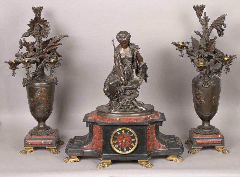 BRONZE SLATE RED MARBLE GARNITURE CLOCK SET DIANA: A magnificent bronze, slate and red marble Victorian garniture clock set circa 1870. Featuring a seated Diana the Huntress and putti drawn chariot. Ht: 24" Width: 22" Depth: 9"