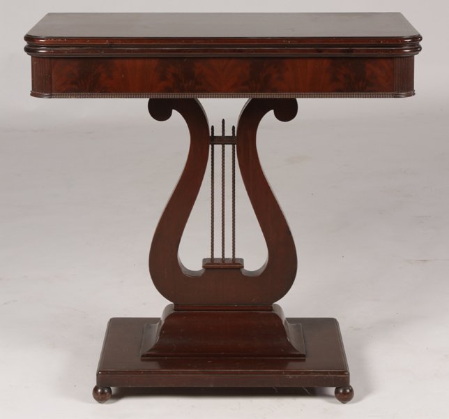 EMPIRE STYLE MAHOGANY FLIP TOP GAMES TABLE: An Empire style mahogany flip top games table having reeded corners and ribbon carved trim circa 1940. Supported on lyre form and plinth base raised on ball feet. Ht: 30" Width: 15.5" Depth: 31"