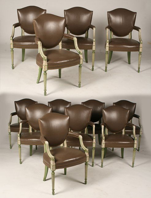 SET 12 CARVED PAINTED ARM CHAIRS MANNER JANSEN: A set of twelve carved and painted shield back dining chairs in the Jansen taste having leather upholstered back and seat circa 1940. Supported on turned and fluted legs. Consisting of all arm chairs.