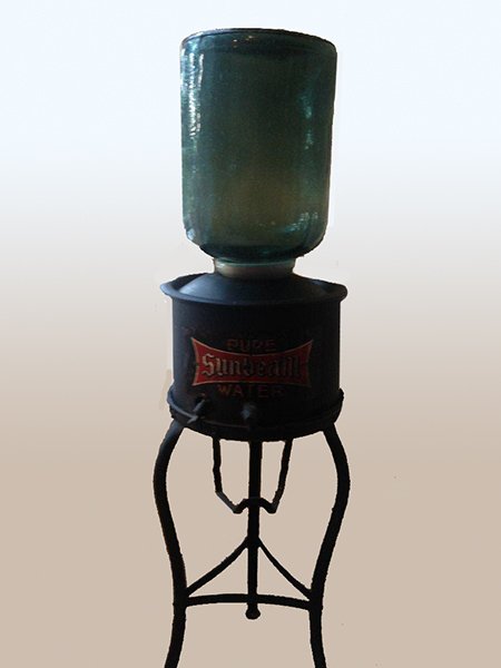 SUNBEAM COOLER TRIPOD METAL STAND: A vintage Sunbeam water cooler having a glass canister resting in its original ceramic conduit base supported on a tripod form metal stand. Ht: 54" Width: 20" Depth: 13"