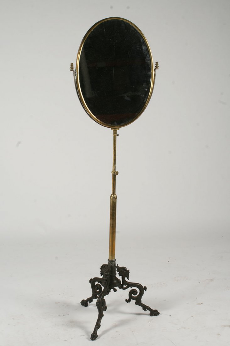 19TH C. ADJUSTABLE BRONZE IRON MIRROR SWIVEL: A nineteenth century adjustable bronze and iron standing mirror having an oval swivel mirror resting on iron griffin form supports. Signed by maker. Ht: 69" Width: 20"