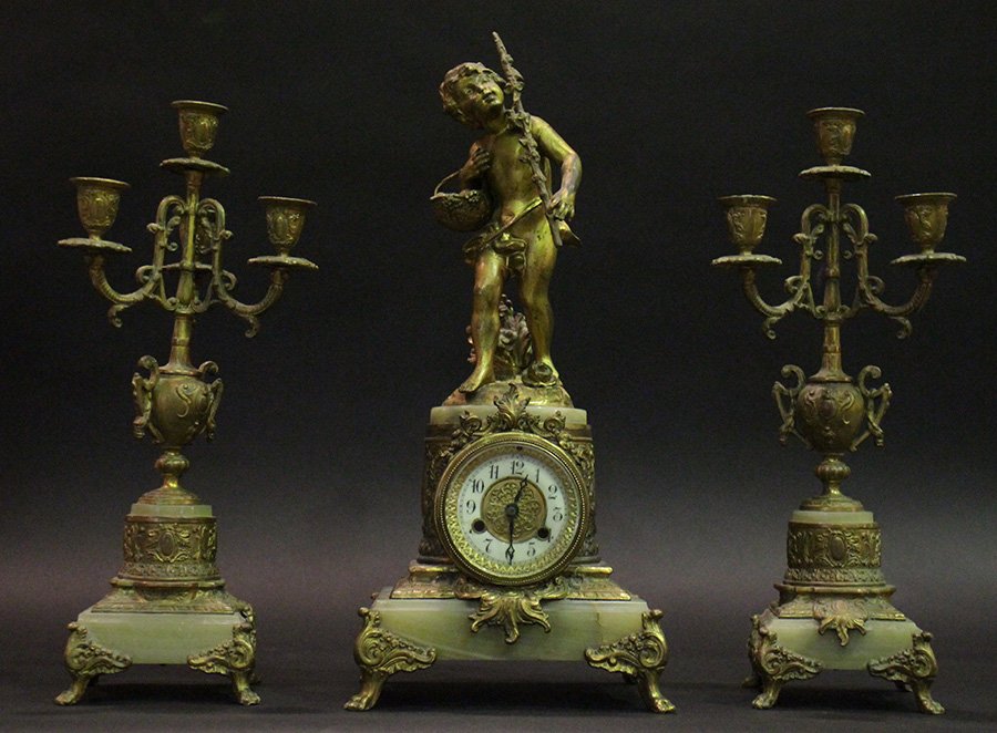 3 PC BRONZE ONYX GARNITURE CLOCK SET 1880: A three piece bronze and onyx garniture clock set having a classically inspired young boy holding a walking stick and fruit basket circa 1880. The clock flanked by urn themed candelabrum. Ht: 9" Width