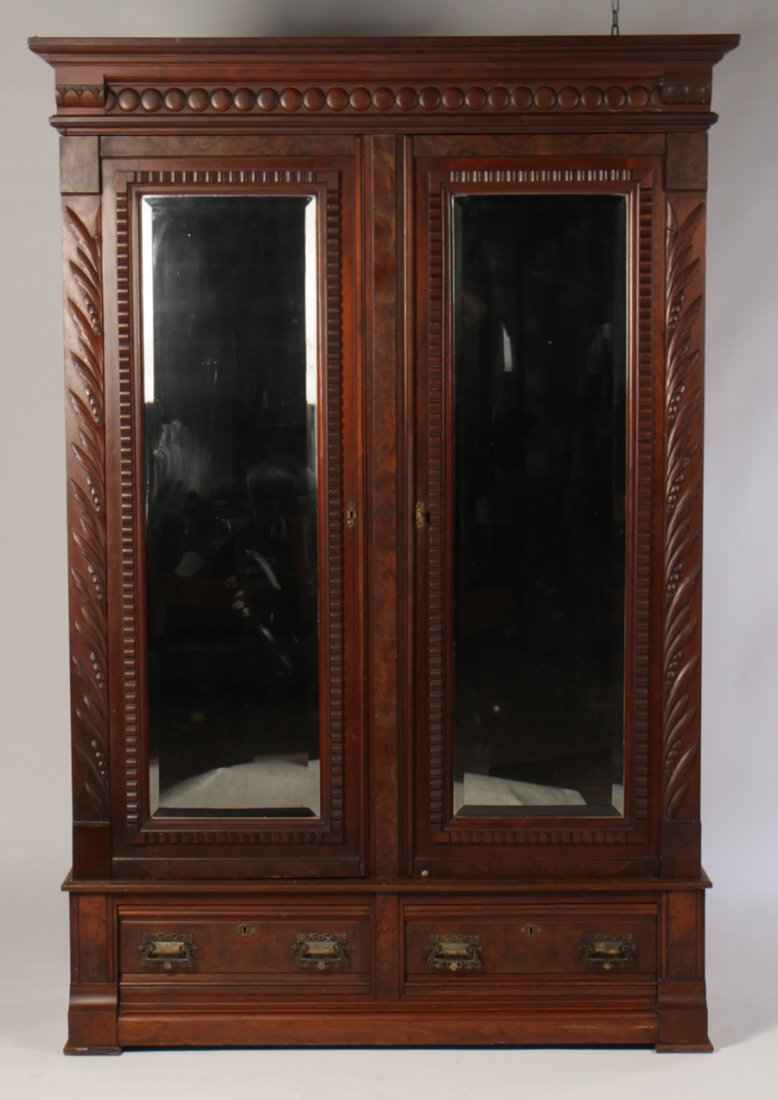 AMER. VICT. CARVED WALNUT ARMOIRE 2 DOORS 1880: American Victorian carved walnut armoire having stepped cornice over pastille form decoration above two beveled mirrored doors circa 1880. All over two drawers. Ht: 89" Width: 57" Depth: 23"