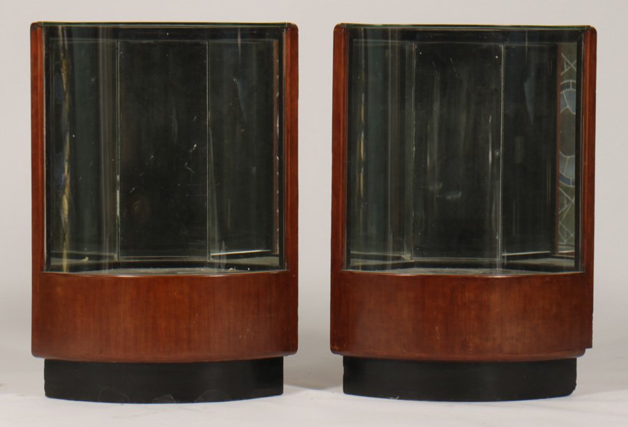 PR SEMI CIRCLE SHOWCASES SHAPED GLASS: A pair of semi-circular showcases having metal edging, and shaped glass all raised on a solid wood base. Ht: 36" Depth: 18"