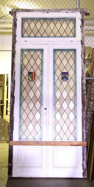 ANTIQUE STAINED GLASS ENTRYWAY: A stained glass entryway with two doors circa 1910. Diamond pattern glass with central shield decoration. Ht: 10' Width: 49" Depth: 5.5"