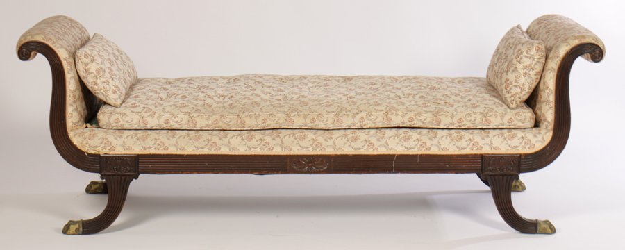 19TH CEN. CARVED MAHOGANY DAYBED UPHOLSTERED: A late nineteenth century carved mahogany classical style daybed having upholstered and rolled ends with reeded wood framing. Over loose cushion and raised on downswept legs with bronze paw form caps.
