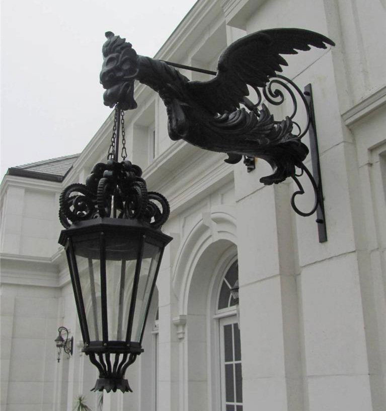 PAIR CAST & WROUGHT IRON GRIFFIN ARCH. SCONCES: A monumental pair of cast and wrought iron architectural sconces having winged griffin figures supporting a Georgian style lantern. Ht: 60" Width: 48"