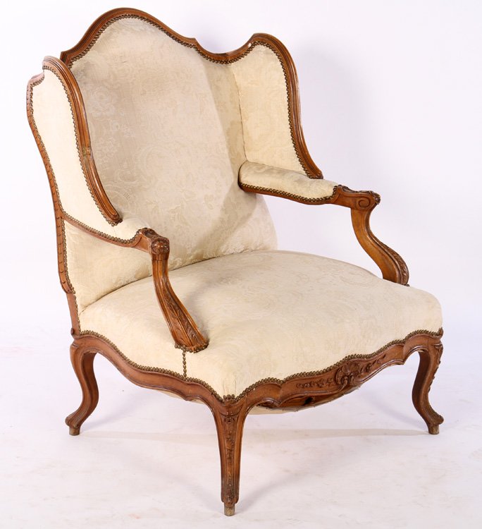 FRENCH CARVED WALNUT BERGERE A OREILLES 1910: A good French carved walnut bergere a oreilles having carved and shaped arms over nailhead trimmed seat circa 1910. All raised on cabriole legs. Ht: 32" Width: 30" Depth: 33" Seat ht:16"