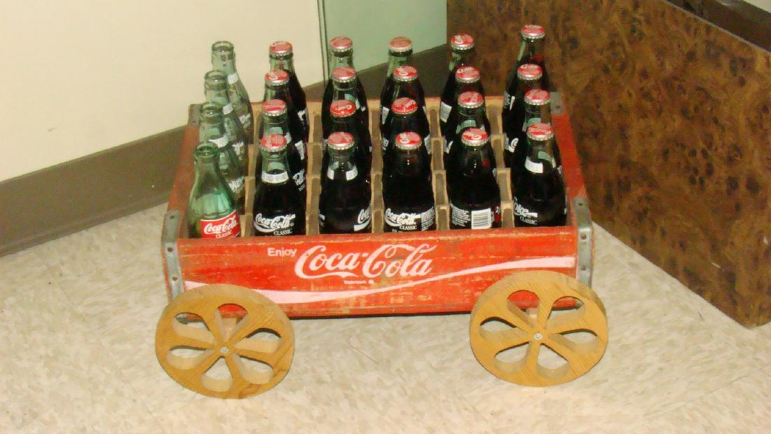 VINTAGE WOODEN WAGON WITH COCA COLA SODA BOTTLES: VINTAGE WOODEN WAGON WITH COCO COLA SODA BOTTLES - ORIGINAL A CRATE FOR DELIVERY OF SODA AND WAS CONVERTED TO A WAGON - WOODEN WHEELS - PAINTED RED - WHEELS ARE NOT ORIGINAL - SIDES HAVE THE COKE EMBL