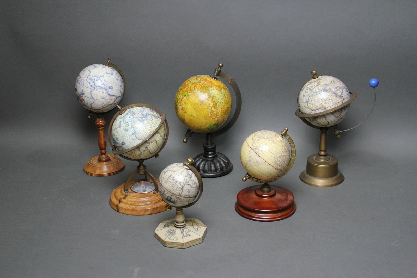 6 MINIATURE GLOBES ON STANDS: Includes faux scrimshaw 7", Compass in wood base 9 1/2" h, brass stand 11" h, 3 on wood stands from 7 1/2" to 11 1/2" h