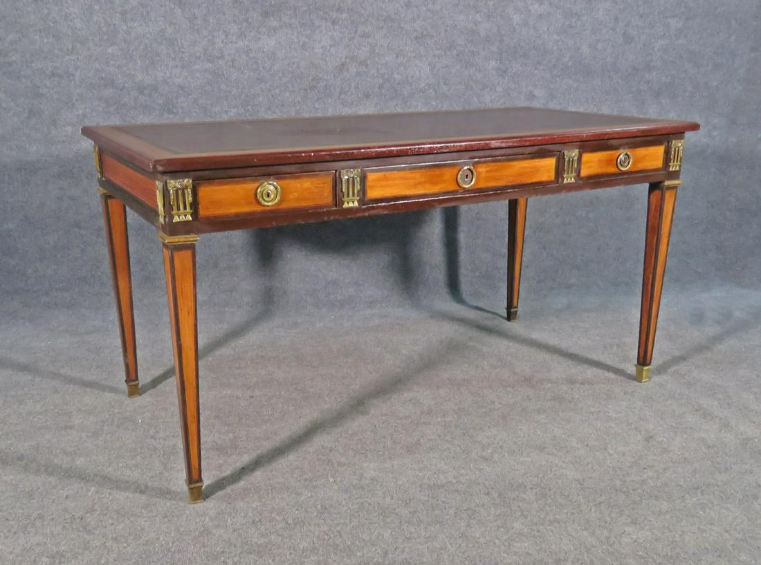 LOUIS XVI STYLE LEATHER TOP DESK: Came out of Waldorf Astoria. Leather top. Walnut and satinwood. Banded. Brass hardware, accents and foot caps. One dovetailed drawer. 29 1/4" h x 57" w x 27 7/8" d.