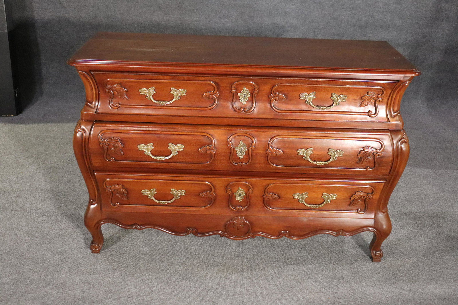 WELLINGTON HALL BOMBAY COMMODE: Carved wood. 3 dovetailed drawers. Brass hardware. 34 1/4" h x 51 7/8" w x 18 1/2" d.