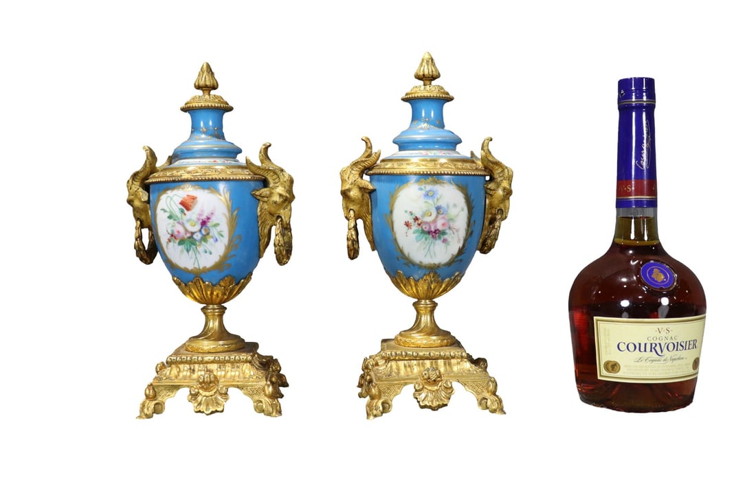 PAIR FRENCH SEVRES STYLE LIDDED PORCELAIN URNS: Gilt bronze mounts. Hand painted. Porcelain. Ram head figural. 11 1/2" h x 6 1/4" w x 4 5/8" d.