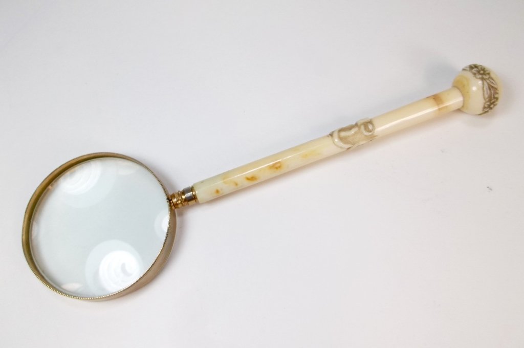 A Japanese Carved Bone Handled Magnifying Glass: An antique Japanese magnifying glass with carved bone handle, having carved relief decoration. Size: 2 1/2" dia. x 8 1/2" L