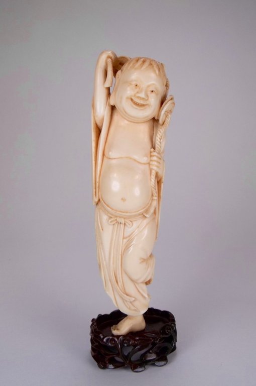 An Antique Chinese Carved Ivory Figure of Liu Hai: A Chinese ivory statue depicting Liuhai holding a chain of money coins, a typical auspicious symbol for wealth and prosperity, affixed to a wooden stand, Ivory without stand approximate 7" tall BIDDER