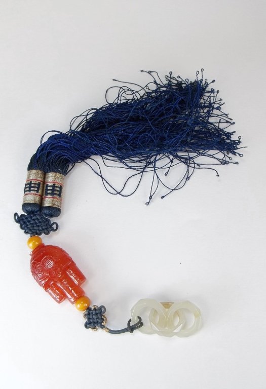A Chinese Carved Jade and Carnelian Tassel: A Chinese tassel comprised of three interlinked jade rings and a well carved red agate carnelian tied to two red beads. dia of each ring approx. 0.75" the length of the carnelian bead approx. 1.75". V