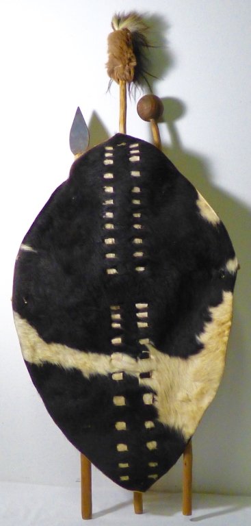 ZULU PEOPLE, SOUTH AFRICA: A hide shield, mounted with iwisa club and assegai spear. Size: 35" L x 21 1/2" W x 50" HProvenance: Property from a Private Collection, Sugar Land, Texas